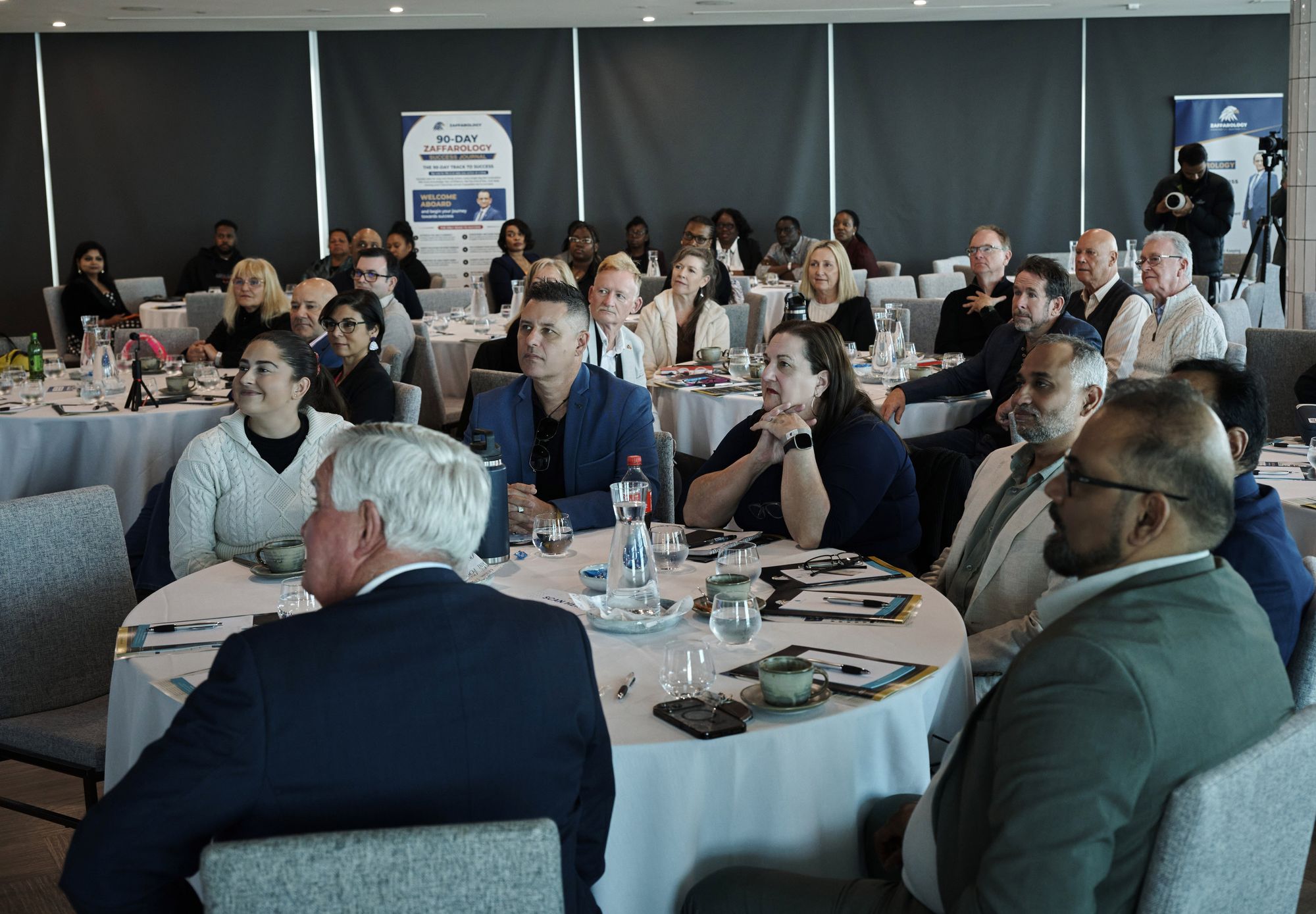 Attendees seated at round tables listening intently during a session