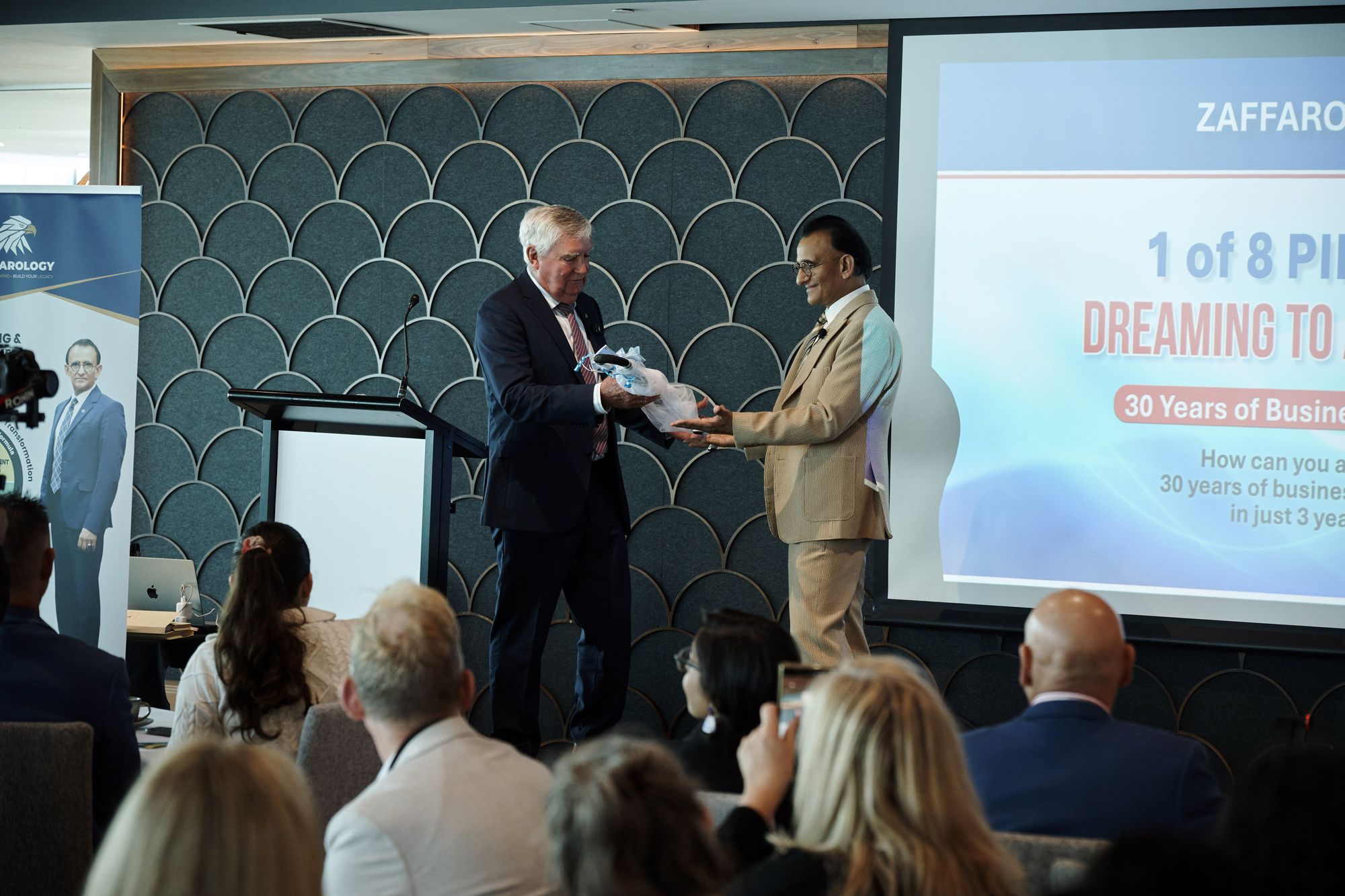 Zaffar Khan presenting a wrapped gift to a guest speaker on stage