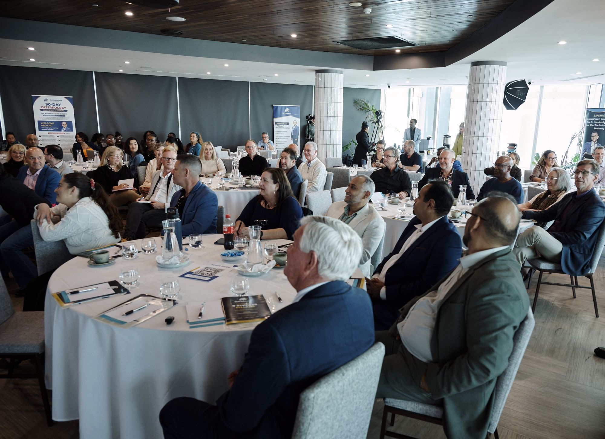 A packed room of attendees at round tables, all turned toward the front