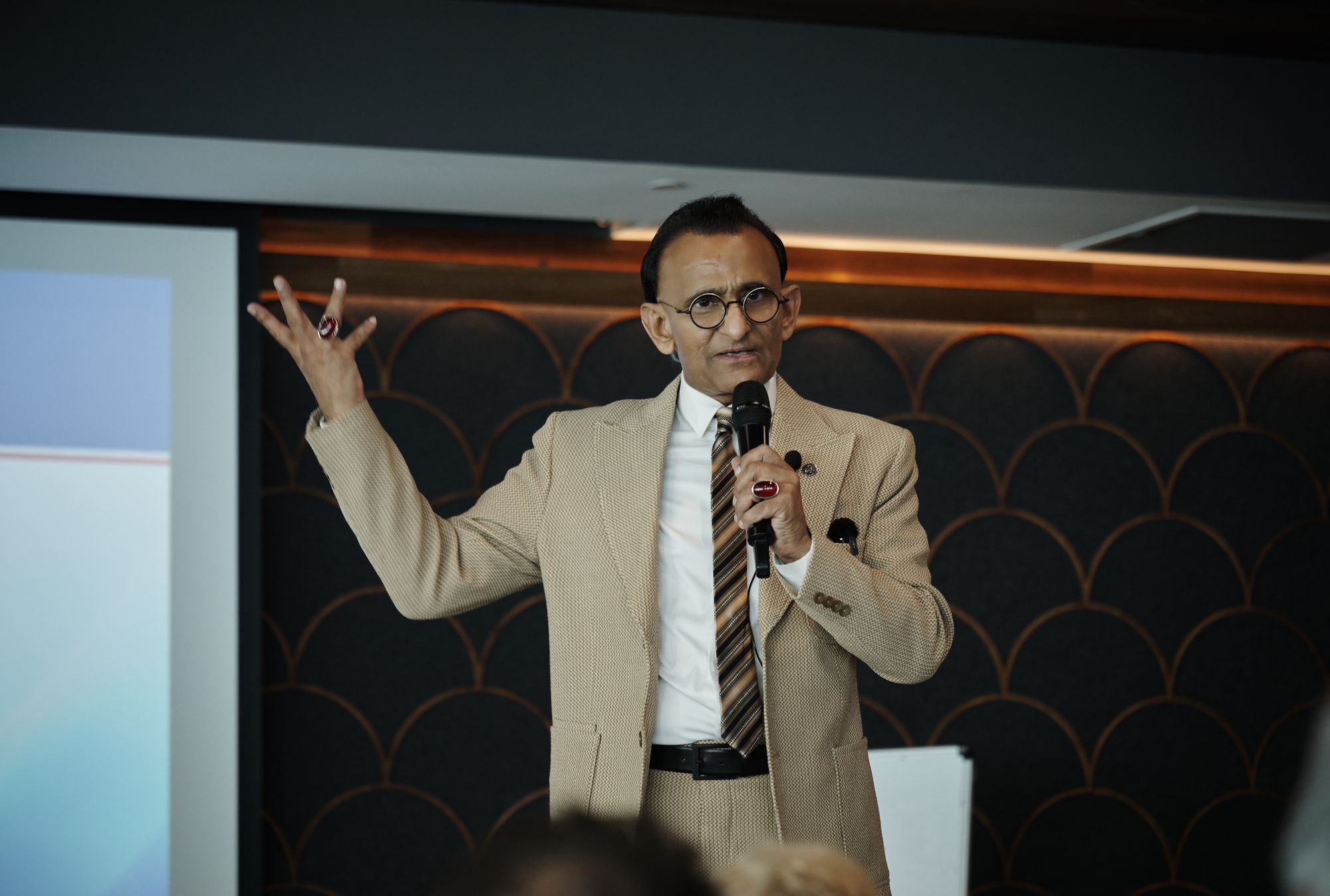 Zaffar Khan with both arms raised, making a point to the room