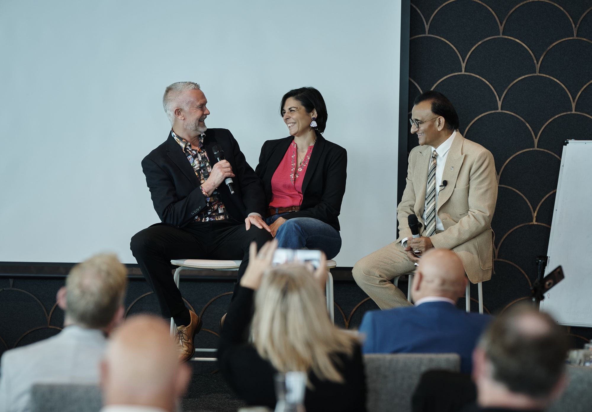 A panel of three seated on stage, one guest speaking into a microphone