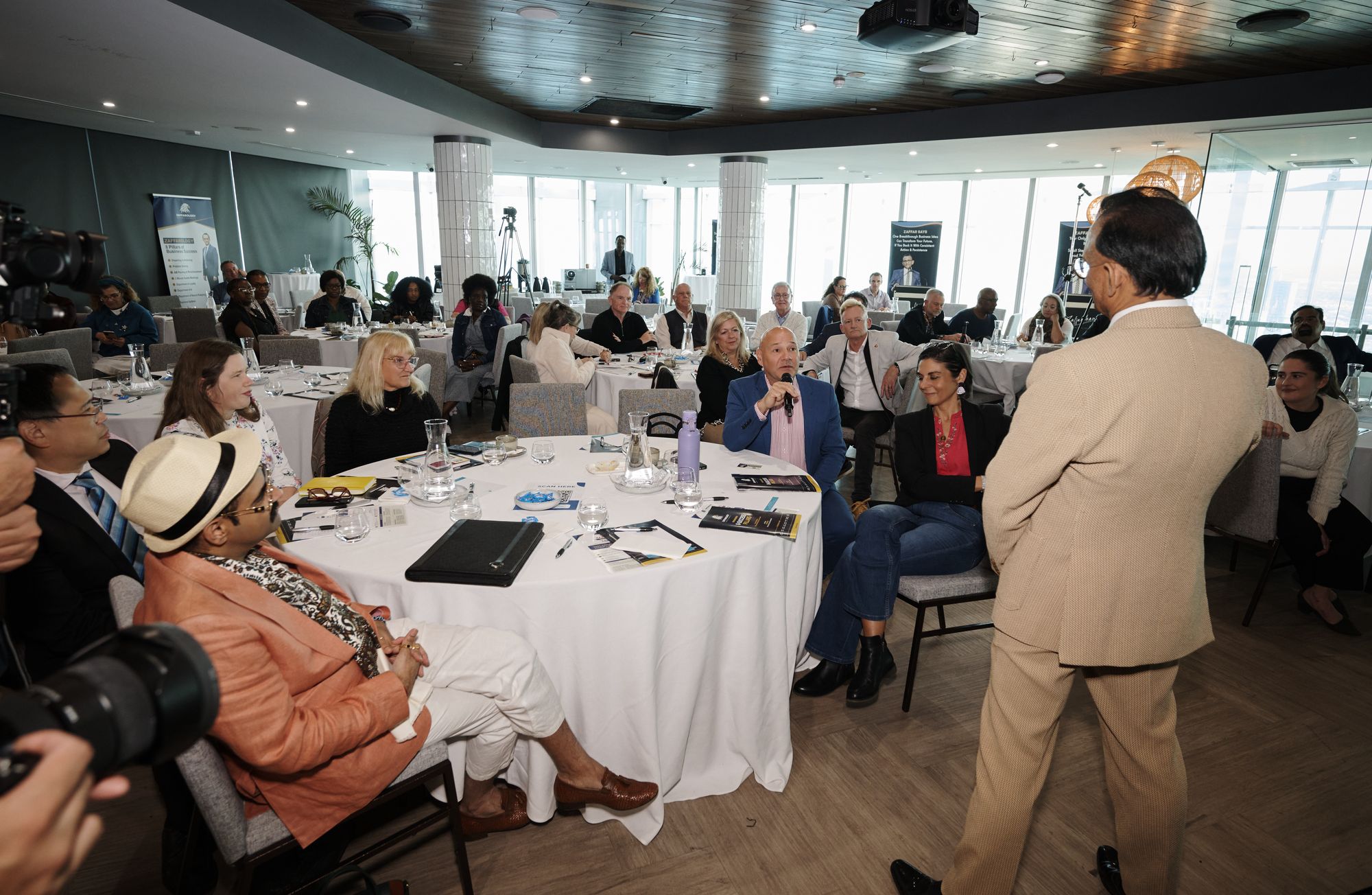Zaffar Khan walking to a table as an attendee speaks into a microphone